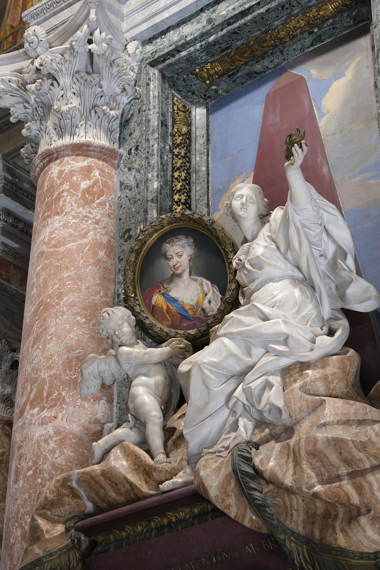 Kolorowe zdjęcie współczesne wnętrza kościoła.  Znajduje się na nim rzeźba. Jest to kobieta w długich szatach. Obok niej mały Amor. Oboje trzymają portret kobiecy. Za rzeźbą kobiety wysoki obelisk i rama. Jest to nagrobek Marii Klementyny Sobieskiej w Bazylice Św. Piotra w Rzymie.