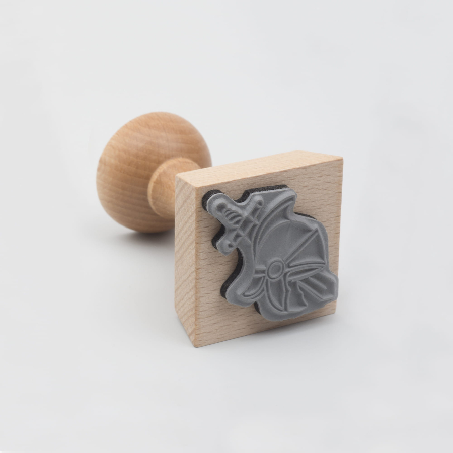 Drewniany stempel z pieczątką w kształcie miecza i hełmu. 
